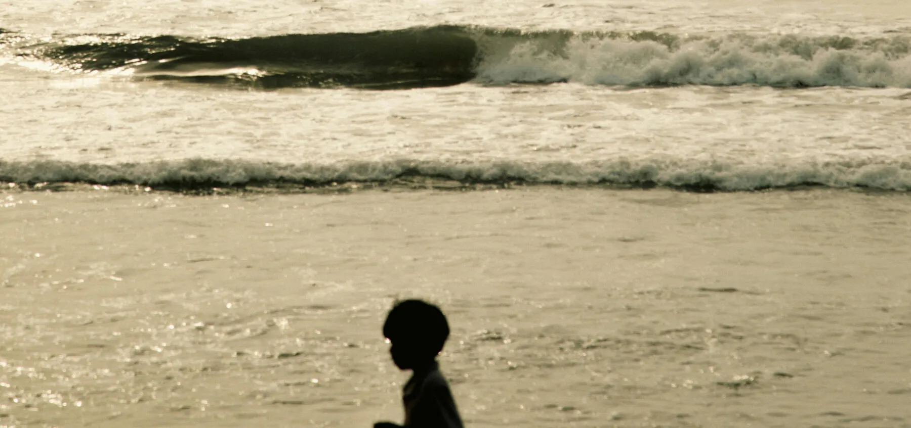 Une silhouette sur la plage devant des vagues dans une lumière dorée.